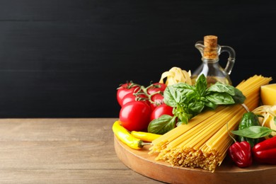 Photo of Raw spaghetti pasta and products on wooden table against black background, closeup. Space for text
