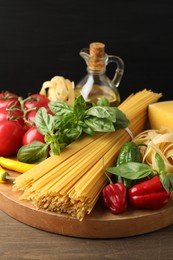 Photo of Different types of raw pasta and products on wooden table against black background, closeup