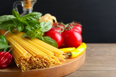 Photo of Raw spaghetti pasta and products on wooden table against black background, closeup