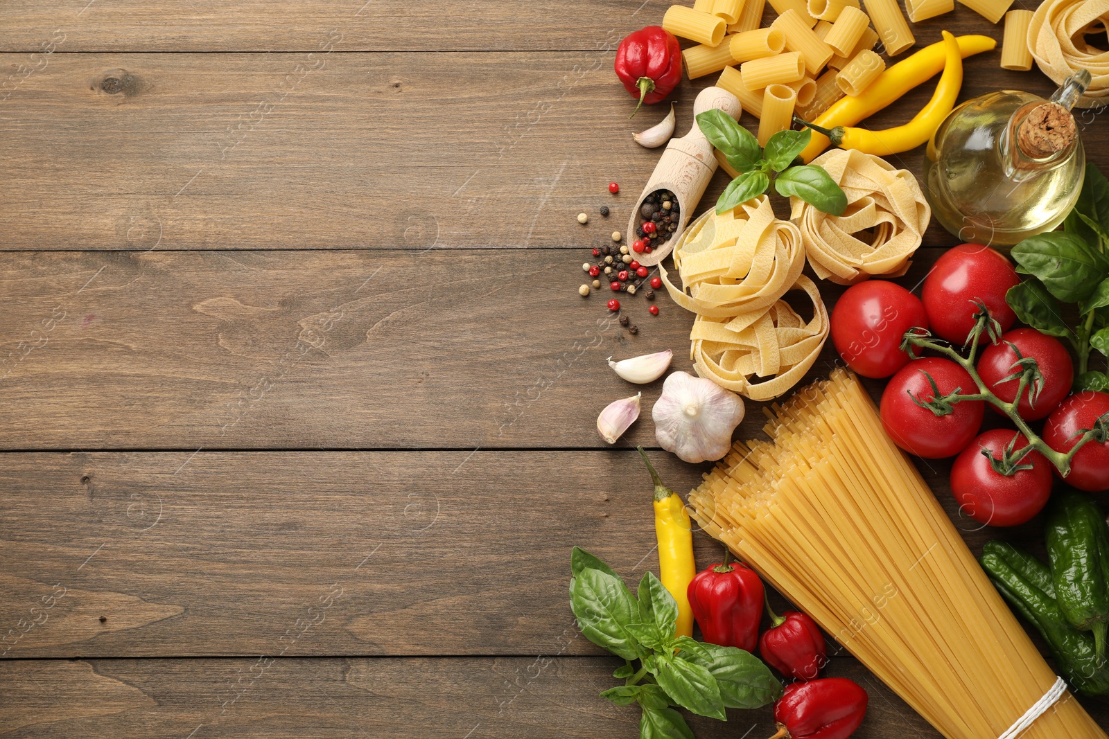 Photo of Different types of raw pasta and products on wooden table, flat lay. Space for text