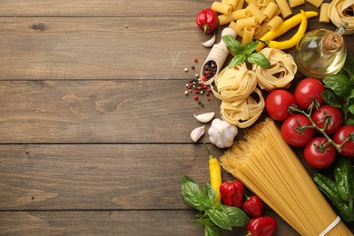 Photo of Different types of raw pasta and products on wooden table, flat lay. Space for text