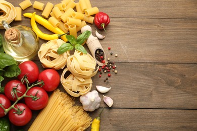 Photo of Different types of raw pasta and products on wooden table, flat lay. Space for text