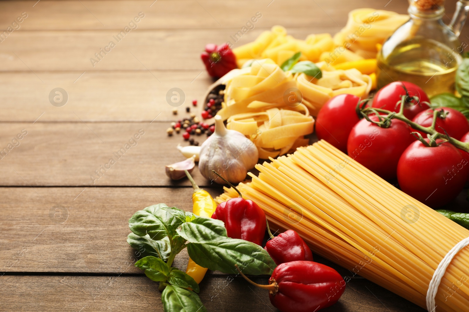 Photo of Different types of raw pasta and products on wooden table, closeup. Space for text