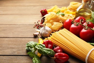 Photo of Different types of raw pasta and products on wooden table, closeup. Space for text