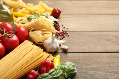 Photo of Different types of raw pasta and products on wooden table, closeup. Space for text
