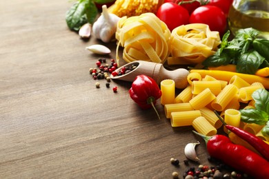 Photo of Different types of raw pasta, products and spices on wooden table, closeup. Space for text