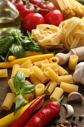Photo of Different types of raw pasta, products and spices on wooden table, closeup