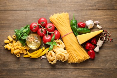 Photo of Different types of raw pasta, products and spices on wooden table, flat lay