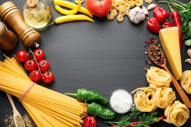 Photo of Frame of different types of raw pasta, products and spices on black wooden table, flat lay. Space for text