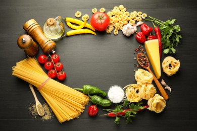 Photo of Frame of different types of raw pasta, products and spices on black wooden table, flat lay. Space for text