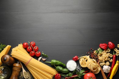 Photo of Different types of raw pasta, products and spices on black wooden table, flat lay. Space for text