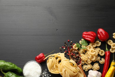 Photo of Different types of raw pasta, products and spices on black wooden table, flat lay. Space for text