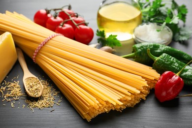 Photo of Raw spaghetti pasta, products and spices on black wooden table, closeup
