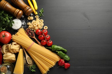 Photo of Different types of raw pasta, products and spices on black wooden table, flat lay. Space for text