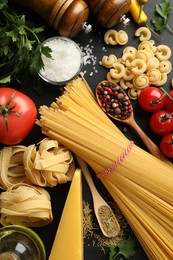 Photo of Different types of raw pasta, products and spices on black wooden table, flat lay