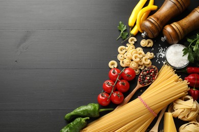 Photo of Different types of raw pasta, products and spices on black wooden table, flat lay. Space for text