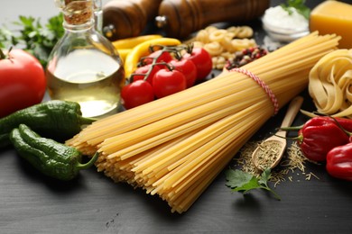 Photo of Different types of raw pasta, products and spices on black wooden table, closeup