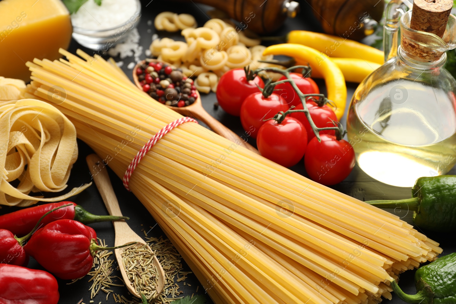 Photo of Different types of raw pasta, products and spices on black wooden table, closeup