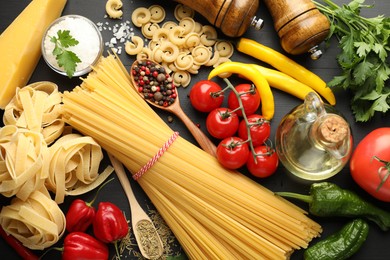 Photo of Different types of raw pasta, products and spices on black wooden table, flat lay