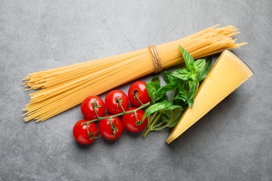 Photo of Raw spaghetti pasta, tomatoes, cheese and basil on grey textured table, flat lay