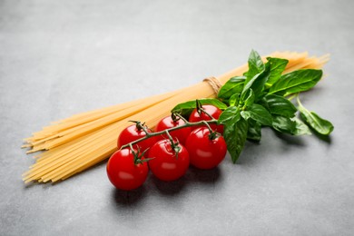 Photo of Raw spaghetti pasta, tomatoes and basil on grey textured table, closeup