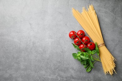 Photo of Raw spaghetti pasta, tomatoes and basil on grey textured table, flat lay. Space for text