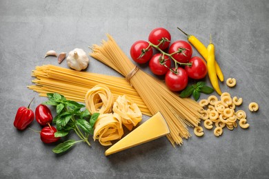 Photo of Different types of raw pasta and products on grey textured table, flat lay