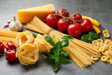 Photo of Different types of raw pasta and products on grey textured table, closeup
