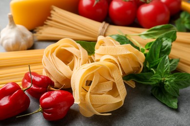 Photo of Different types of raw pasta and products on grey textured table, closeup