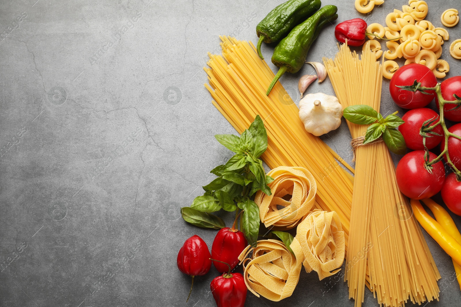 Photo of Different types of raw pasta and products on grey textured table, flat lay. Space for text