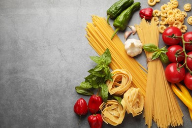 Photo of Different types of raw pasta and products on grey textured table, flat lay. Space for text