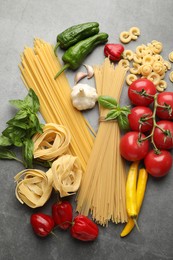 Photo of Different types of raw pasta and products on grey textured table, flat lay