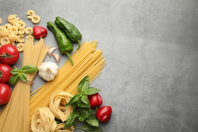 Photo of Different types of raw pasta and products on grey textured table, flat lay. Space for text