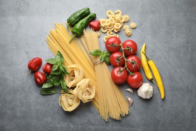 Photo of Different types of raw pasta and products on grey textured table, flat lay