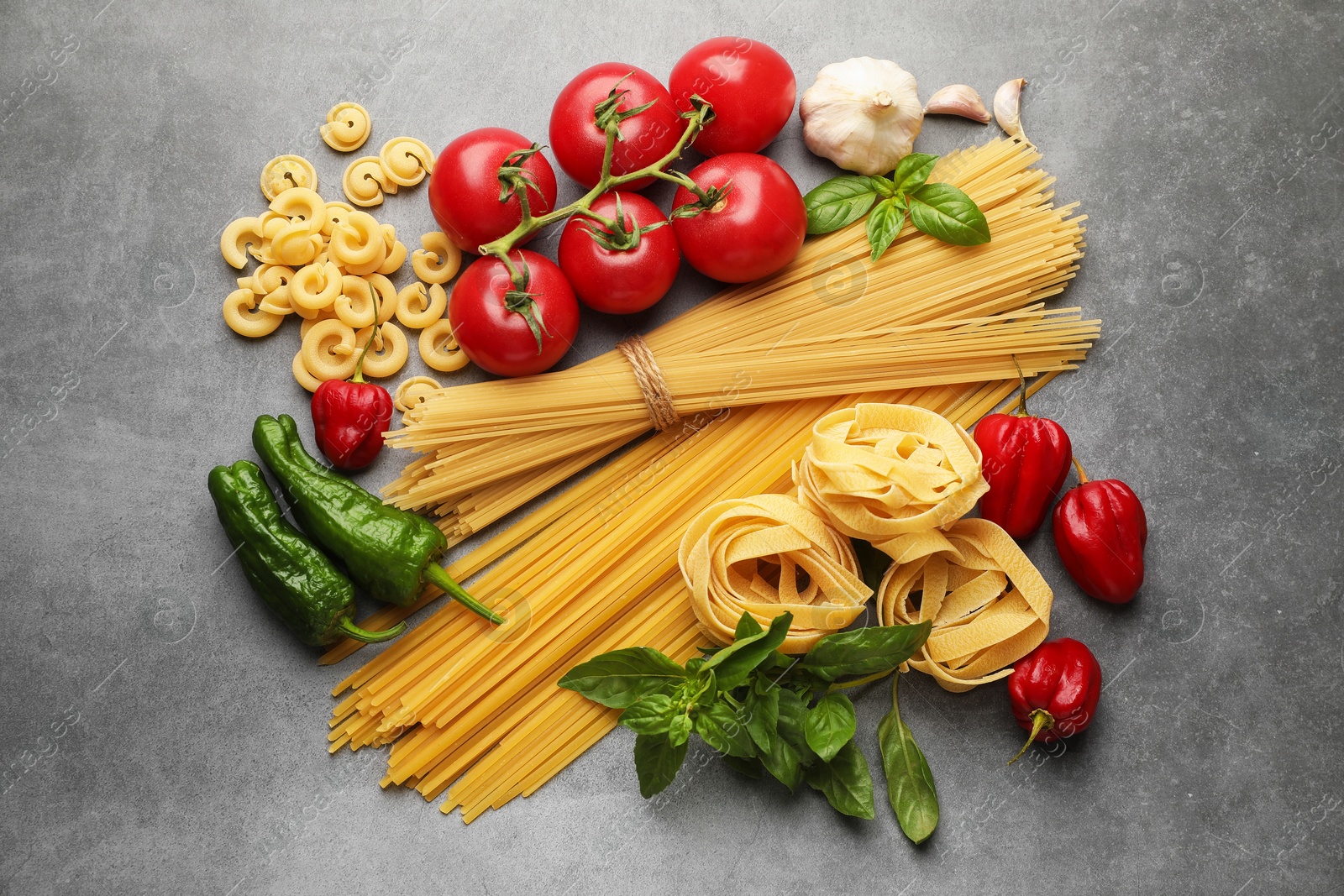 Photo of Different types of raw pasta and products on grey textured table, flat lay
