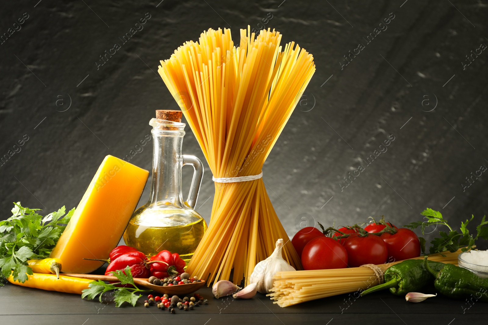 Photo of Raw spaghetti pasta, products and spices on black wooden table against dark textured background