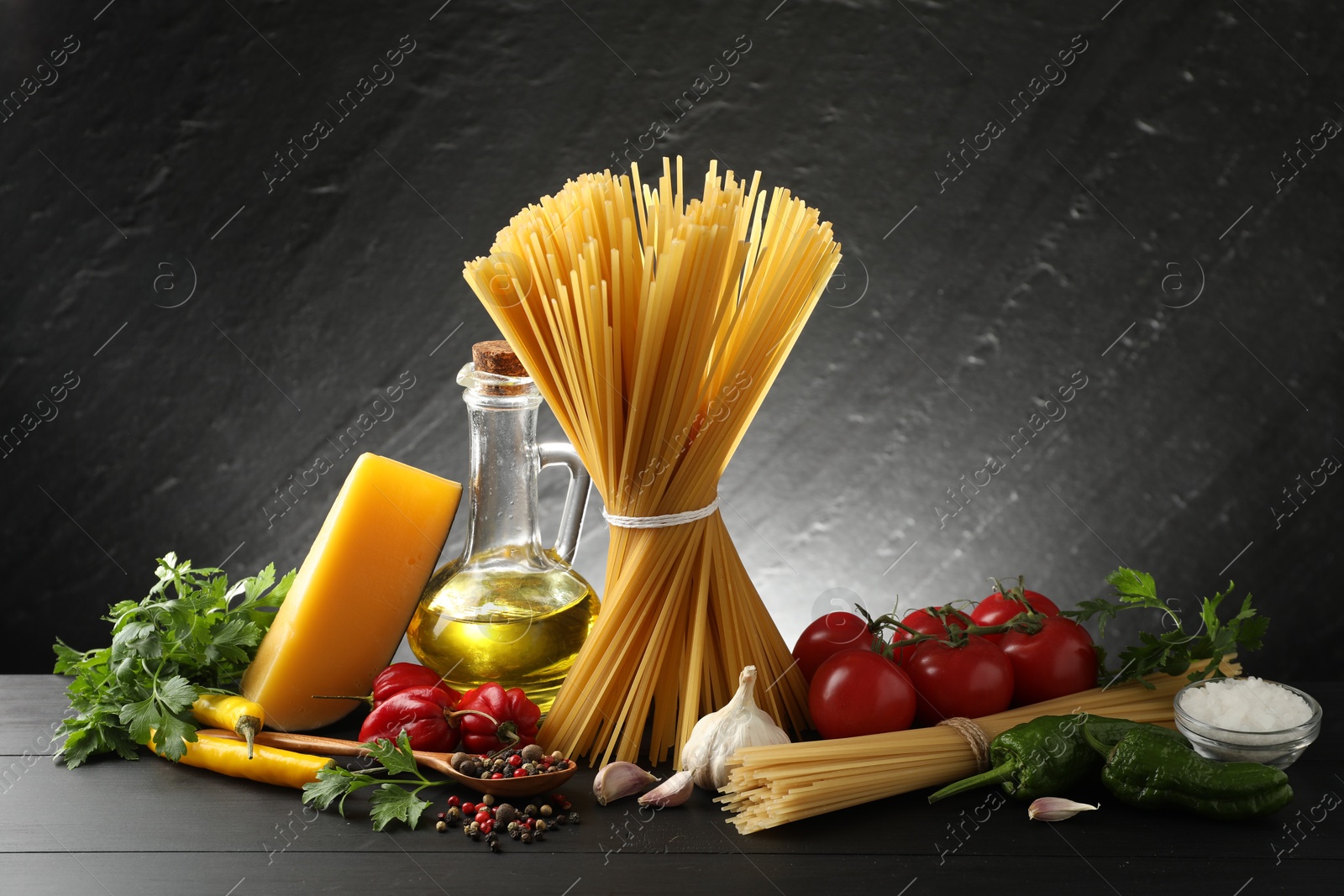 Photo of Raw spaghetti pasta, products and spices on black wooden table against dark textured background