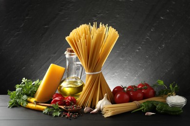 Photo of Raw spaghetti pasta, products and spices on black wooden table against dark textured background