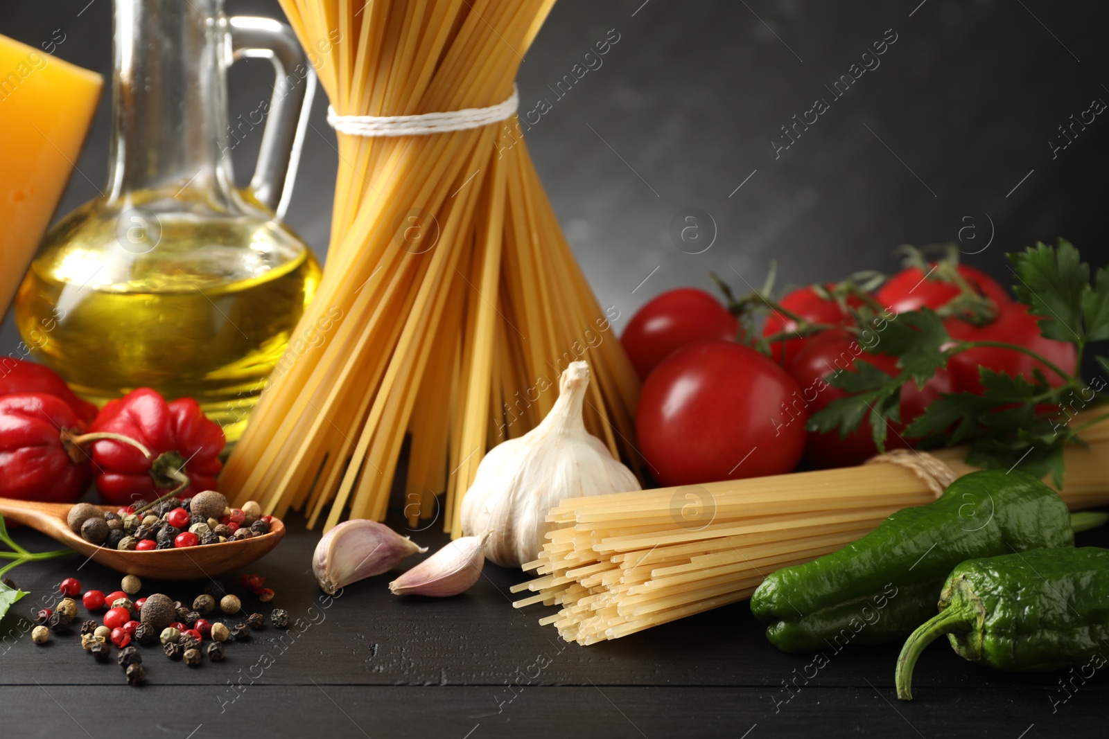 Photo of Raw spaghetti pasta, products and spices on black wooden table against dark background, closeup