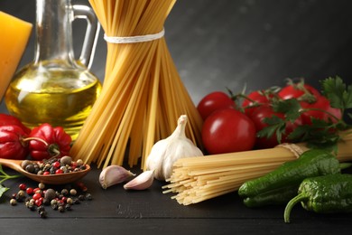 Photo of Raw spaghetti pasta, products and spices on black wooden table against dark background, closeup