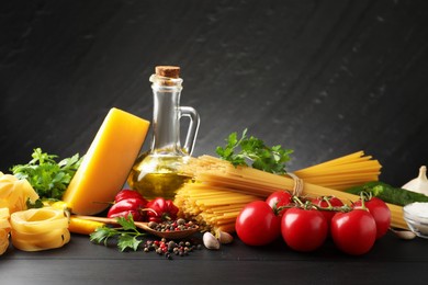 Photo of Different types of raw pasta, products and spices on black wooden table against dark textured background
