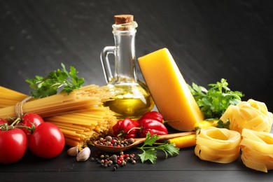 Photo of Different types of raw pasta, products and spices on black wooden table against dark textured background, closeup