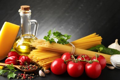 Photo of Raw spaghetti pasta, products and spices on black table against dark textured background, closeup