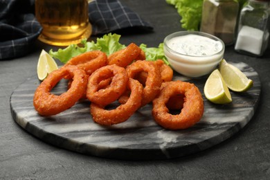 Photo of Fried squid rings served with sauce on black table, closeup
