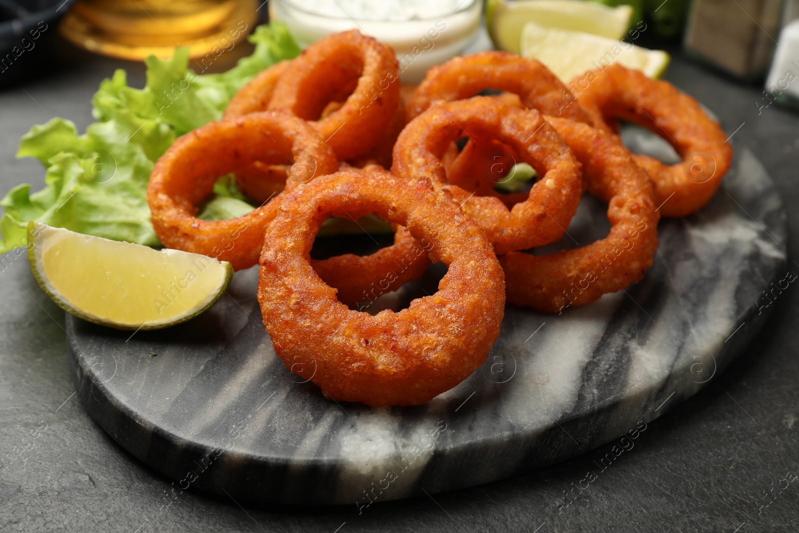 Photo of Fried squid rings, lime and lettuce on black table, closeup