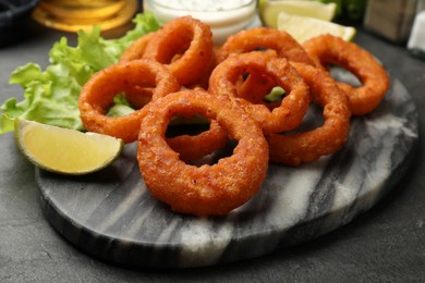 Photo of Fried squid rings, lime and lettuce on black table, closeup