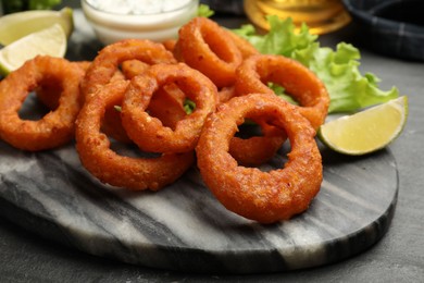 Photo of Fried squid rings, lime, lettuce and sauce on black table, closeup