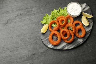 Photo of Fried squid rings served with sauce on black table, top view. Space for text