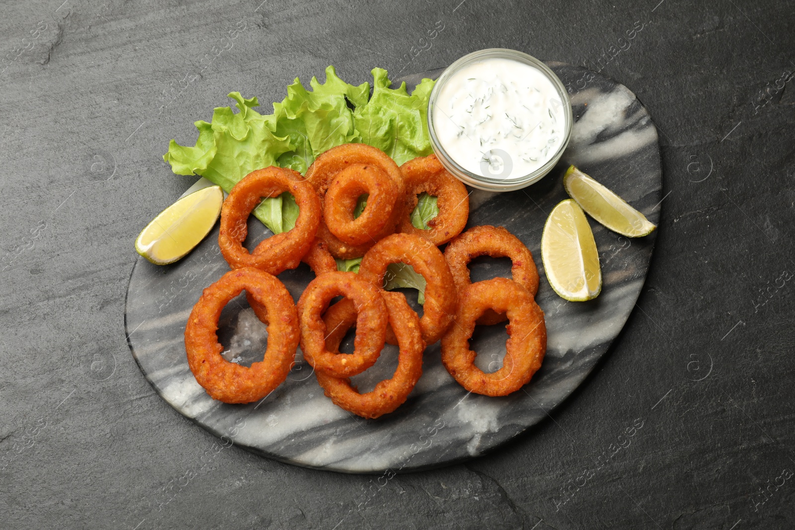 Photo of Fried squid rings served with sauce on black table, top view