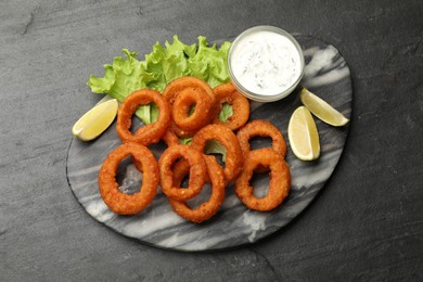 Photo of Fried squid rings served with sauce on black table, top view